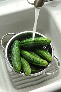 Mini cucumbers being washing in a bowl in a white sink